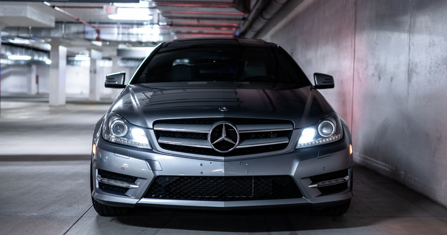 Front view of a silver Mercedes-Benz C-Class with headlights on in a parkade