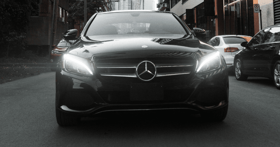 Front view of a black Mercedes-Benz C-Class with headlights on, parked on a city street