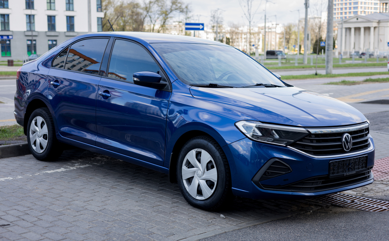 Blue Volkswagen sedan parked on a city street with buildings in the background.