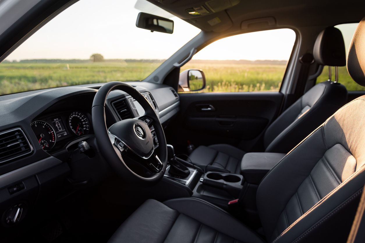 Interior of a Volkswagen vehicle showing steering wheel, dashboard, and leather seats with sunlight coming through the window.