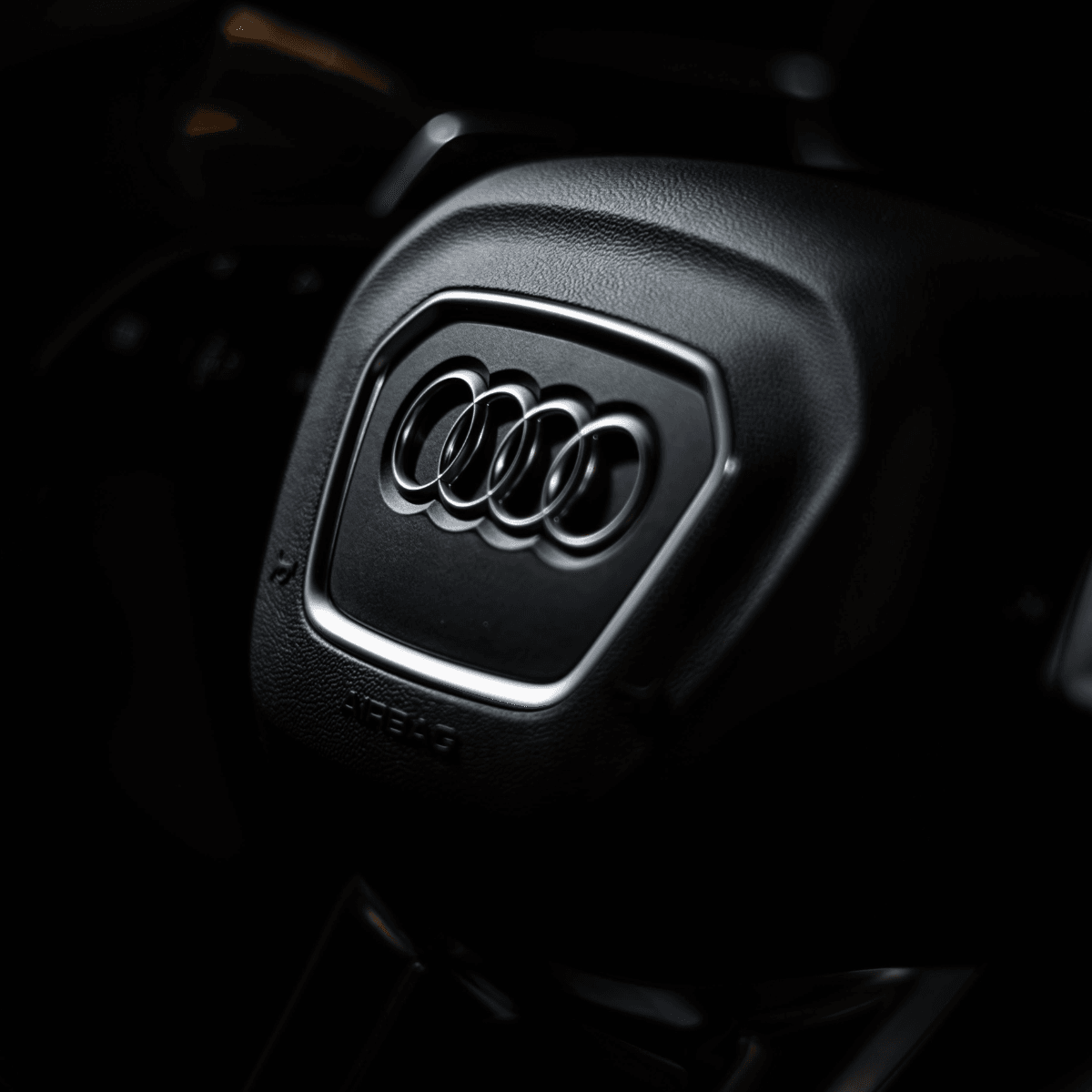   Close-up of the four-ring Audi logo on a black leather steering wheel