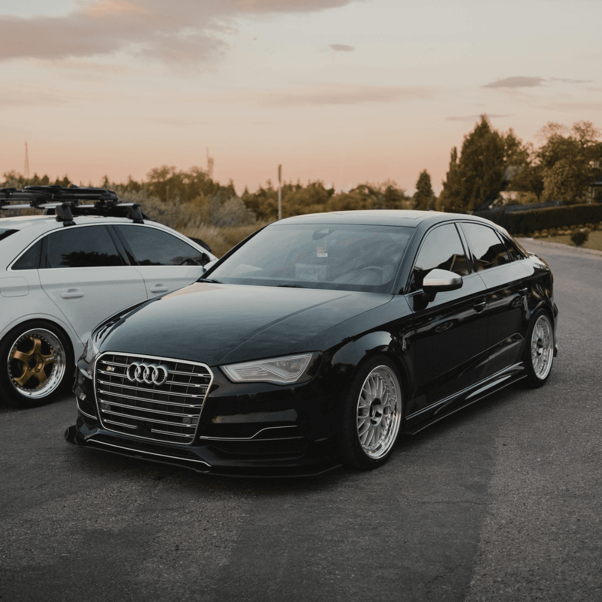 Black Audi S3 sedan on lowered suspension with silver BBS-style wheels at a car meet during golden hour