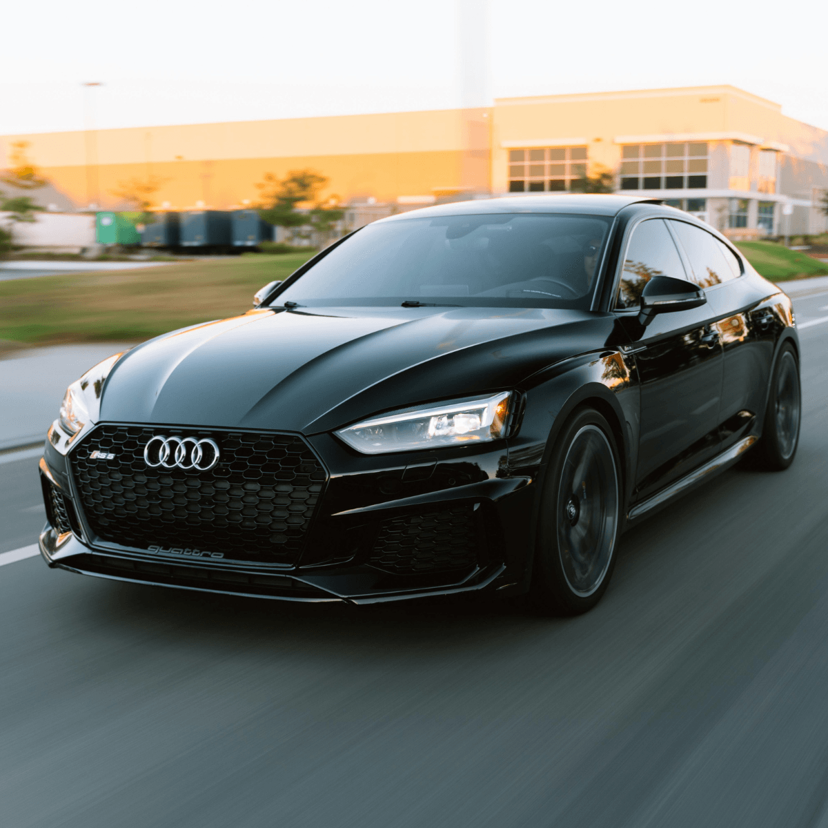 Black Audi RS5 Sportback with quattro badge driving on a road at dusk, shot from a low front angle