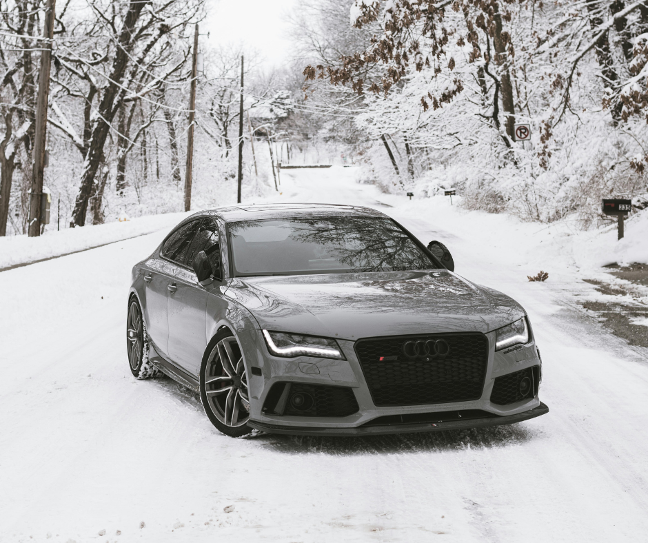 Silver Audi RS7 performance sedan on snow-covered residential street lined with winter trees