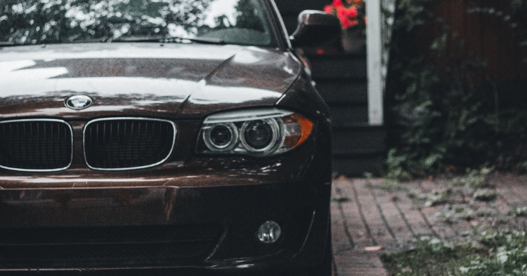 Front end of a dark brown BMW with round headlights parked on a brick driveway