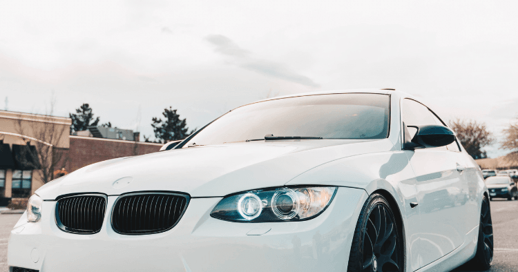 White BMW coupe with illuminated headlights and black wheels parked in a lot