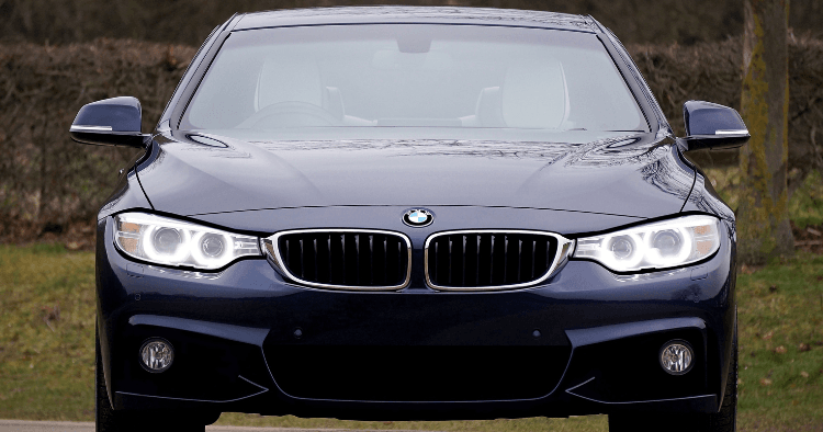 Front view of a dark blue BMW 4 Series with glowing headlights parked on a lawn