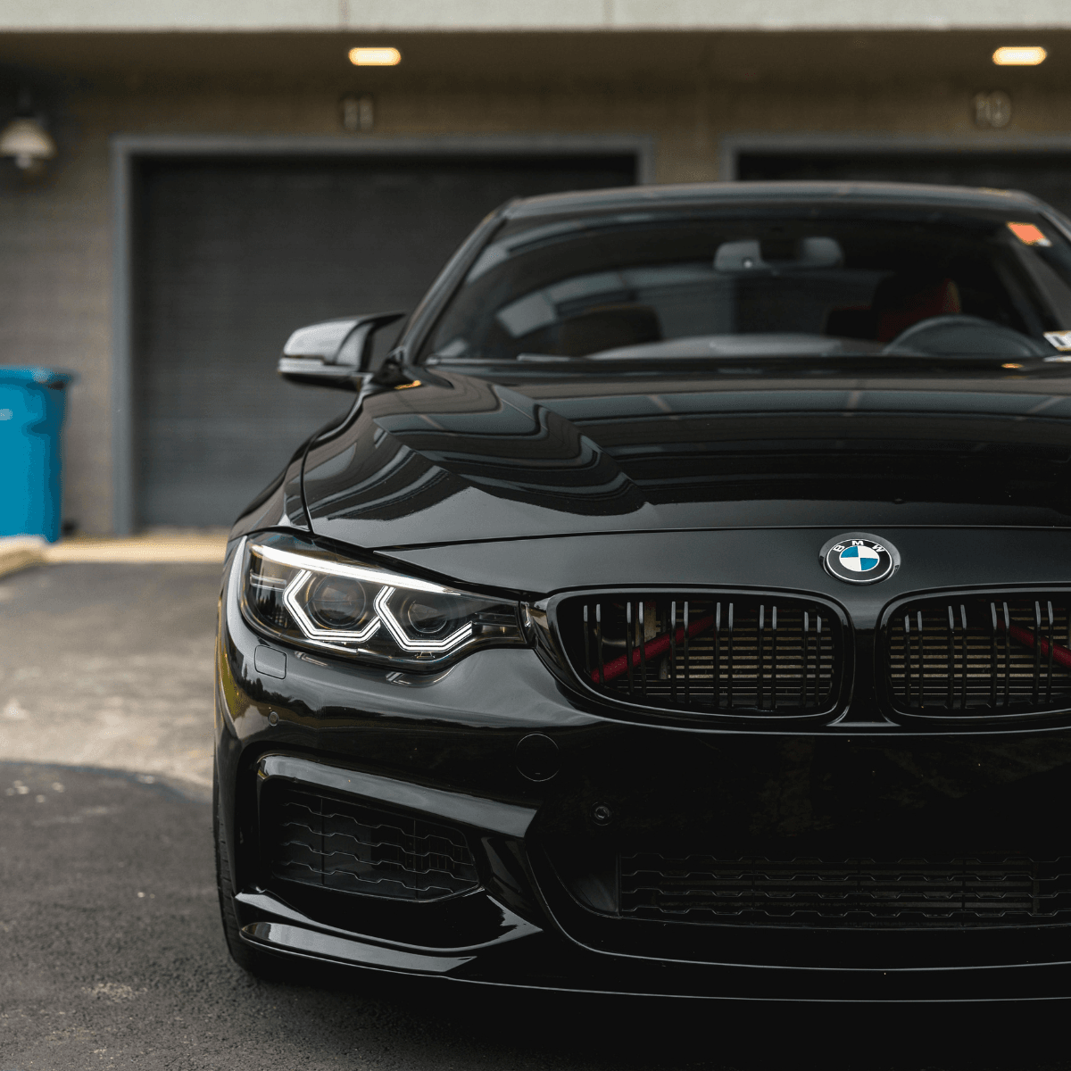 Front view of a black BMW 4 Series parked in front of garage doors, showcasing the kidney grille and LED headlights