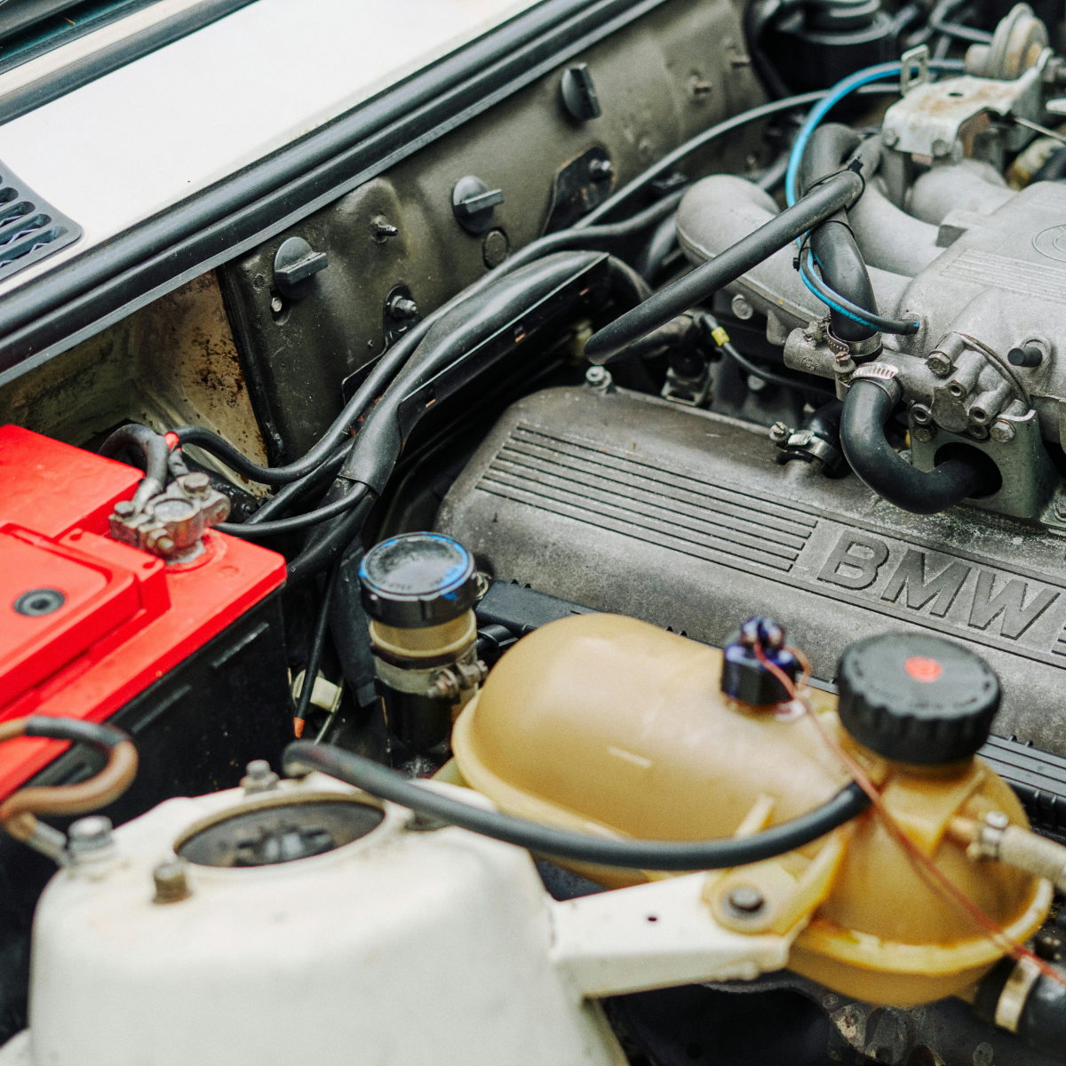 Open engine bay of a classic BMW showing the battery, fluid reservoirs, and inline engine block
