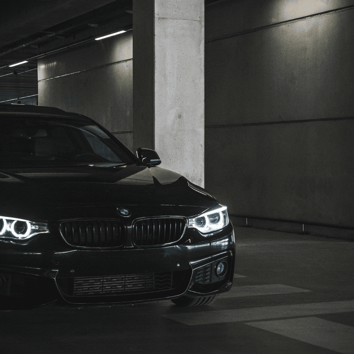 Black BMW 3 Series with illuminated angel eye headlights parked inside a parkade