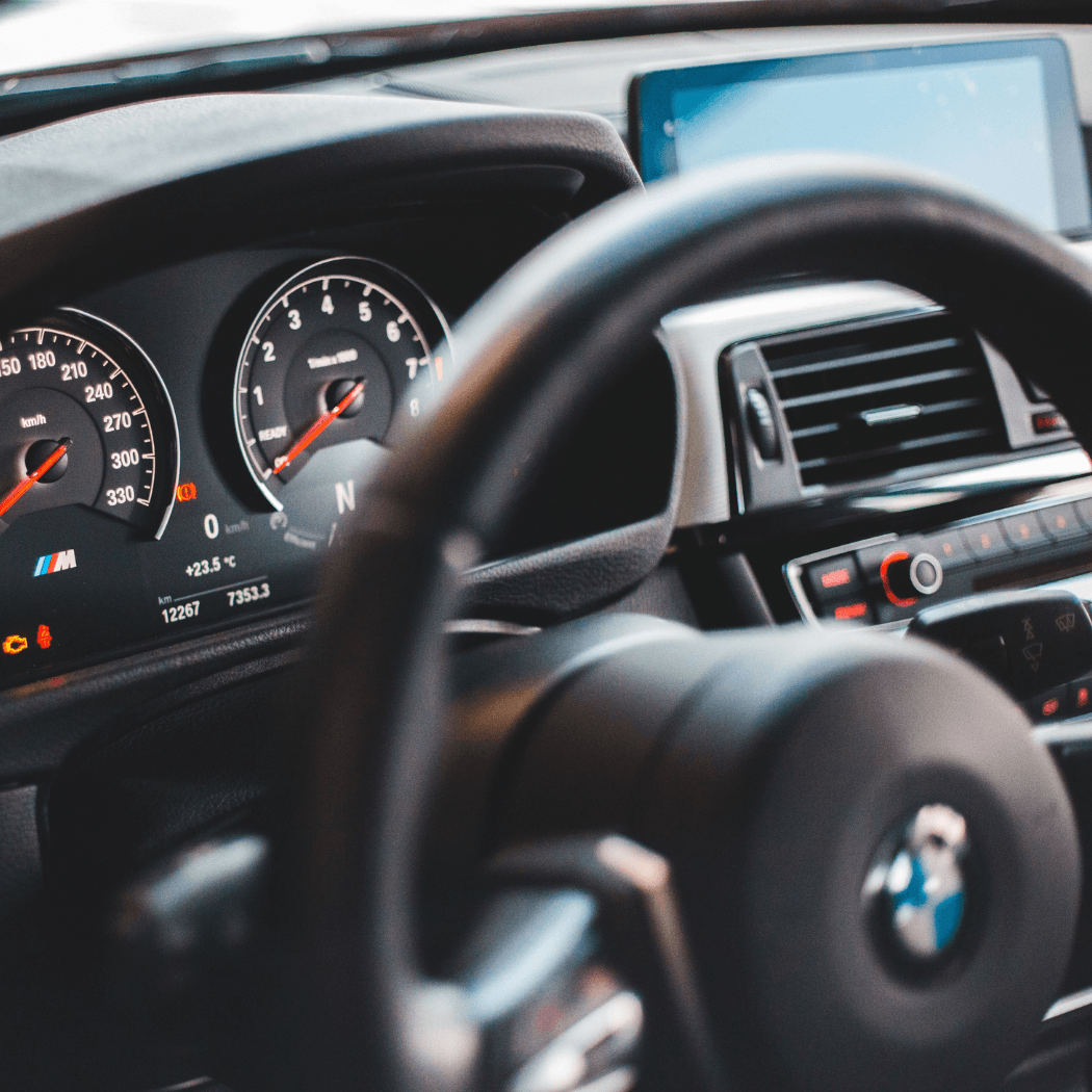 Close-up of a BMW M Series instrument cluster showing the speedometer reaching 330 km/h, tachometer, and digital display reading 23.5°C, with the steering wheel and infotainment screen visible in the background.