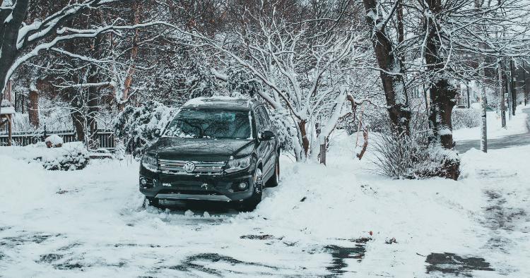 Black Volkswagen Tiguan parked on a snowy residential street beneath snow-covered trees