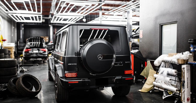 Black Mercedes G-Wagon AMG parked rear-facing inside an auto repair shop.