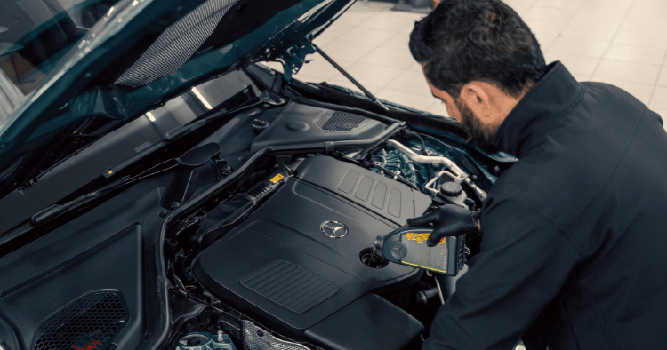 Mechanic checking oil level under the hood of a dark green Mercedes engine.
