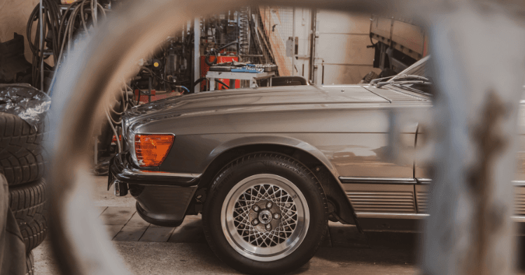 Vintage silver Mercedes convertible seen through a round tool rack in a shop.