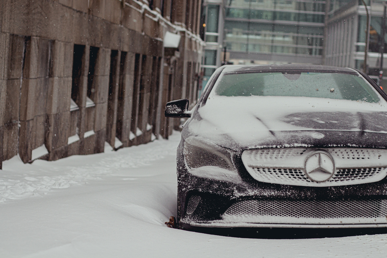 Mercedes-Benz sedan covered in snow and parked on a city street during winter