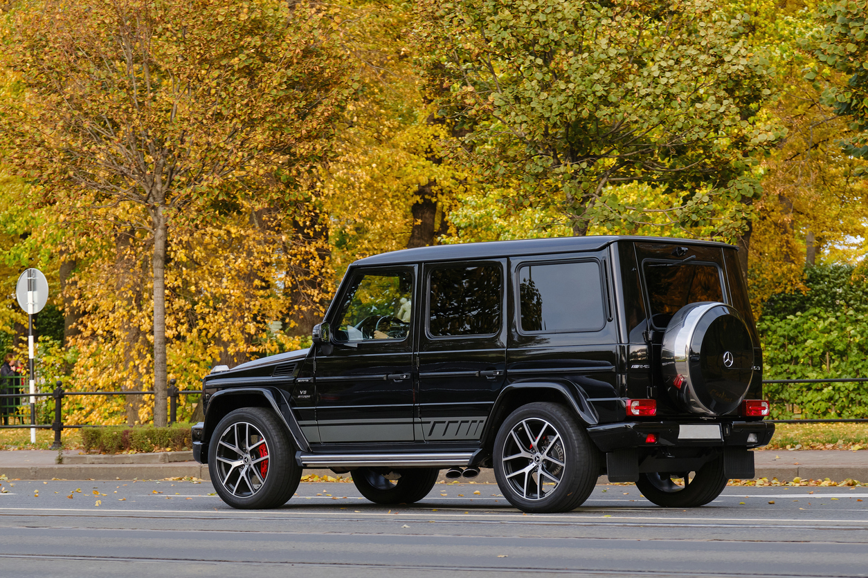 Black Mercedes-Benz G-Class SUV parked on a street with autumn trees in the background