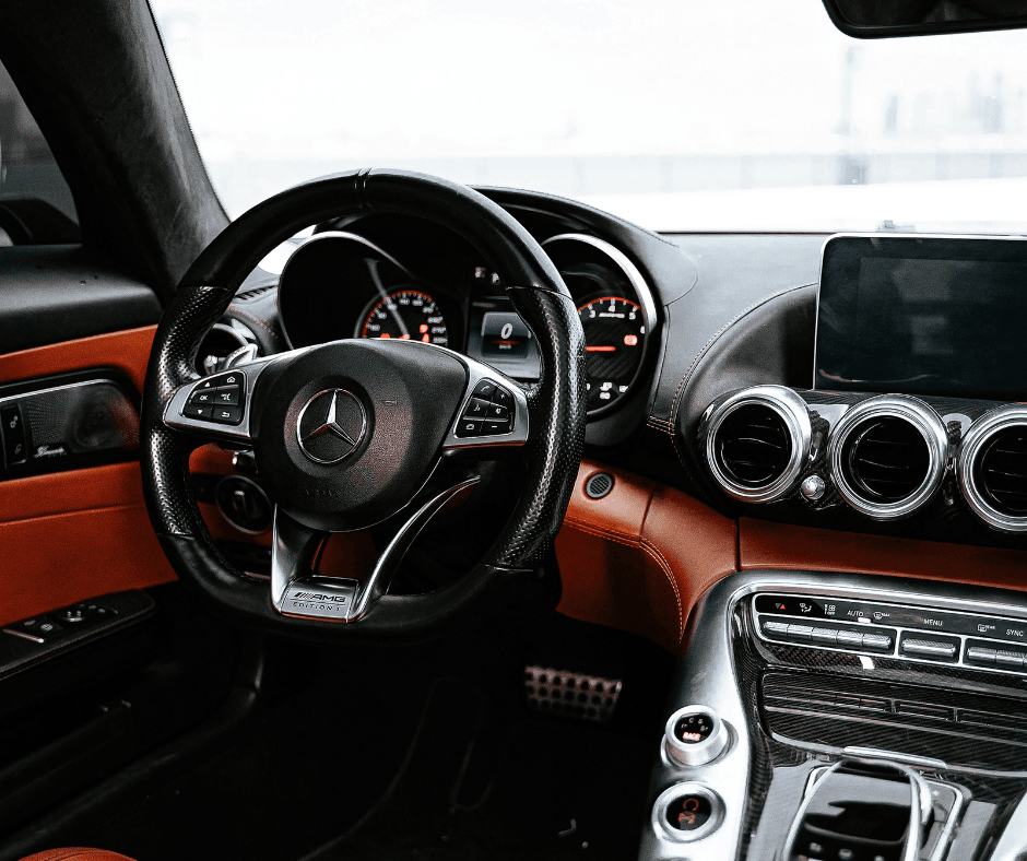 Interior of a Mercedes-AMG featuring a perforated leather steering wheel with AMG Edition badge, red and black cabin trim, carbon fibre accents, and a digital instrument cluster.