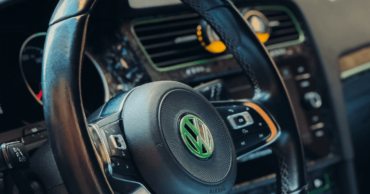 Close-up of a Volkswagen steering wheel badge lit green against the dashboard.