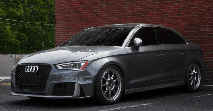 Grey Audi RS3 sedan with black wheels parked against a brick wall